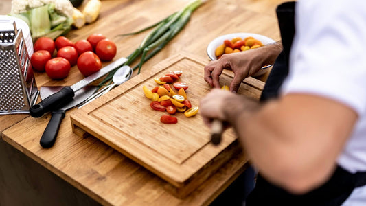 A left-handed chef slicing fresh vegetables on a wooden cutting board.