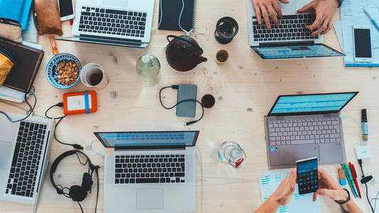 Several people working on laptops at a shared desk, viewed from above.