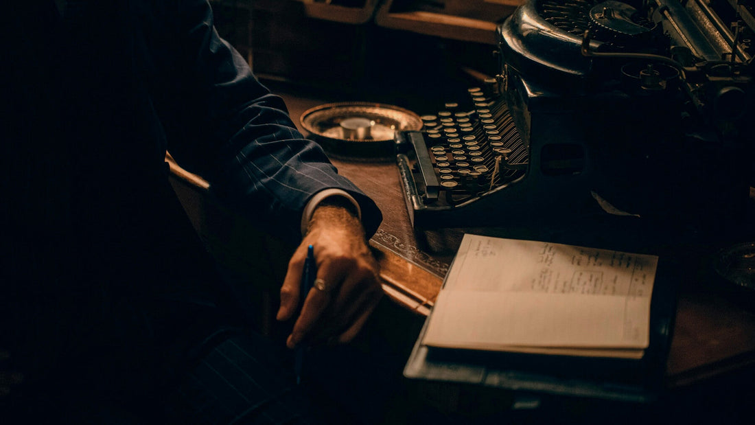 Left-handed writer holding a pen beside a vintage typewriter, symbolizing creativity and the legacy of left-handed authors.