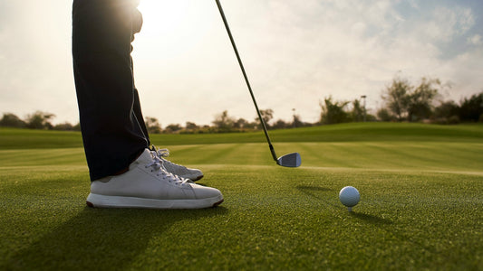 The feet of a left-handed golfer preparing to take a put shot.