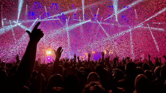 Packed concert crowd glowing under colorful lights at a live show.