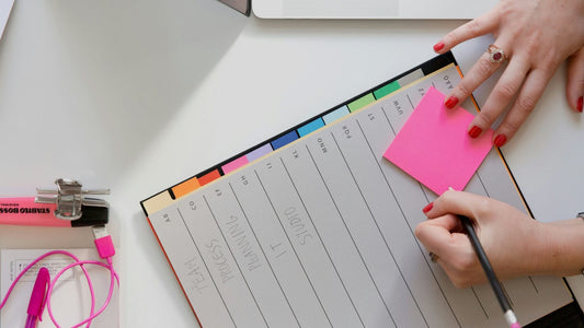 Close-up of a left hand writing a note on a sticky note.