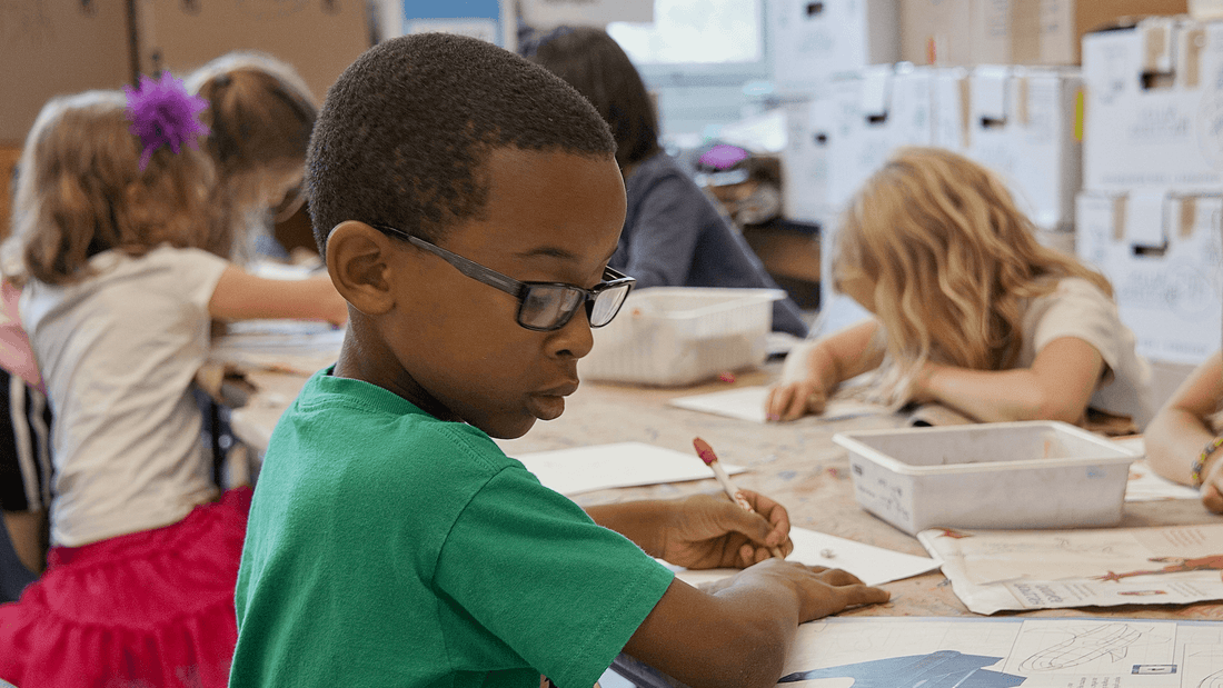 Young left-handed child writing at a classroom desk with a pencil during a school lesson
