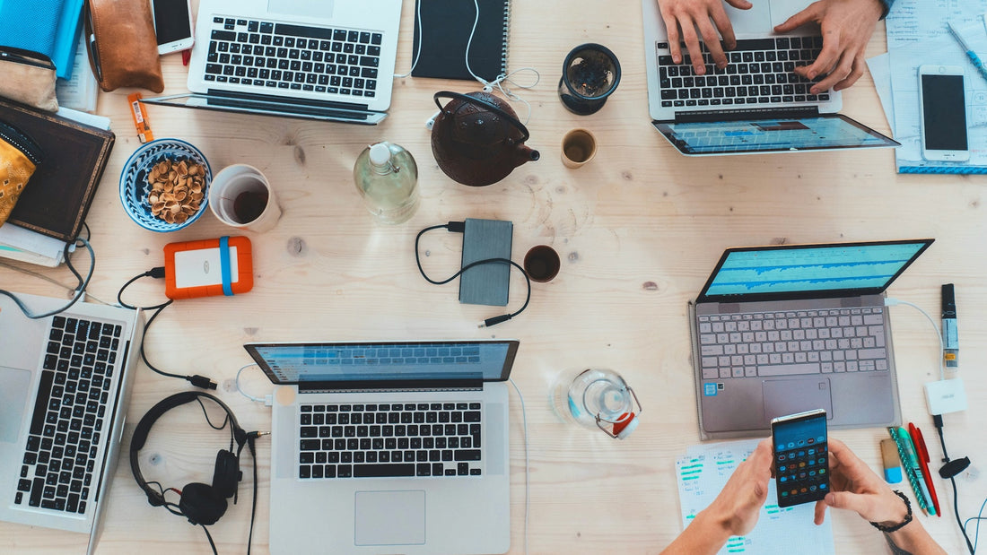 Several people working on laptops at a shared desk, viewed from above.