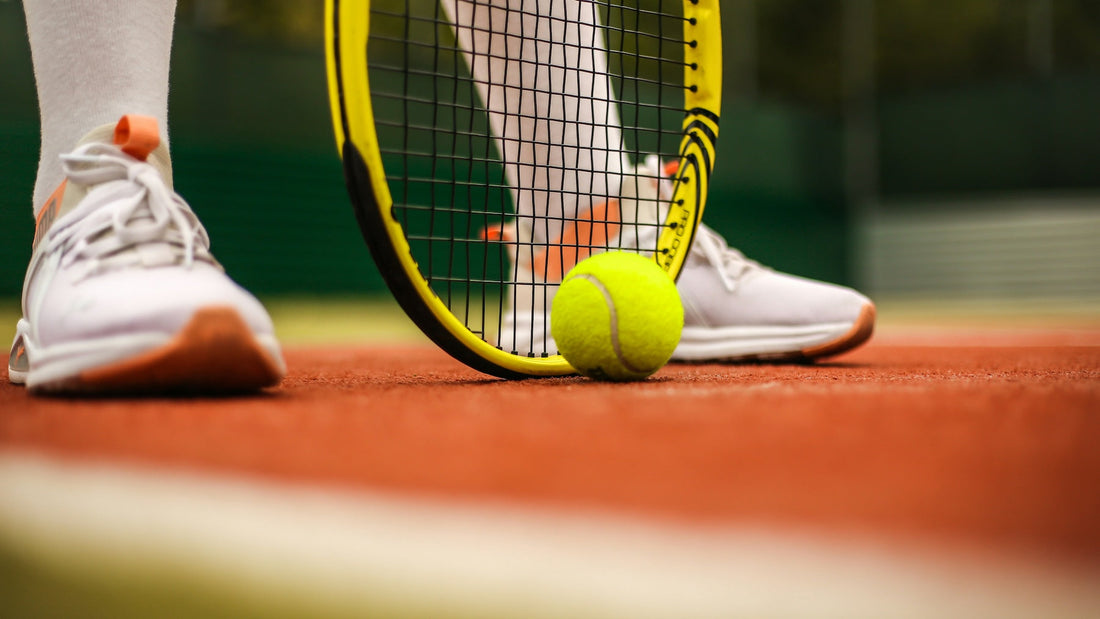 Close-up of a tennis player’s feet on red clay court, with a racket and ball, highlighting the unique perspective of a southpaw player.