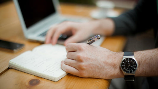 Close-up of a man wearing a wristwatch writing left-handed in a journal.